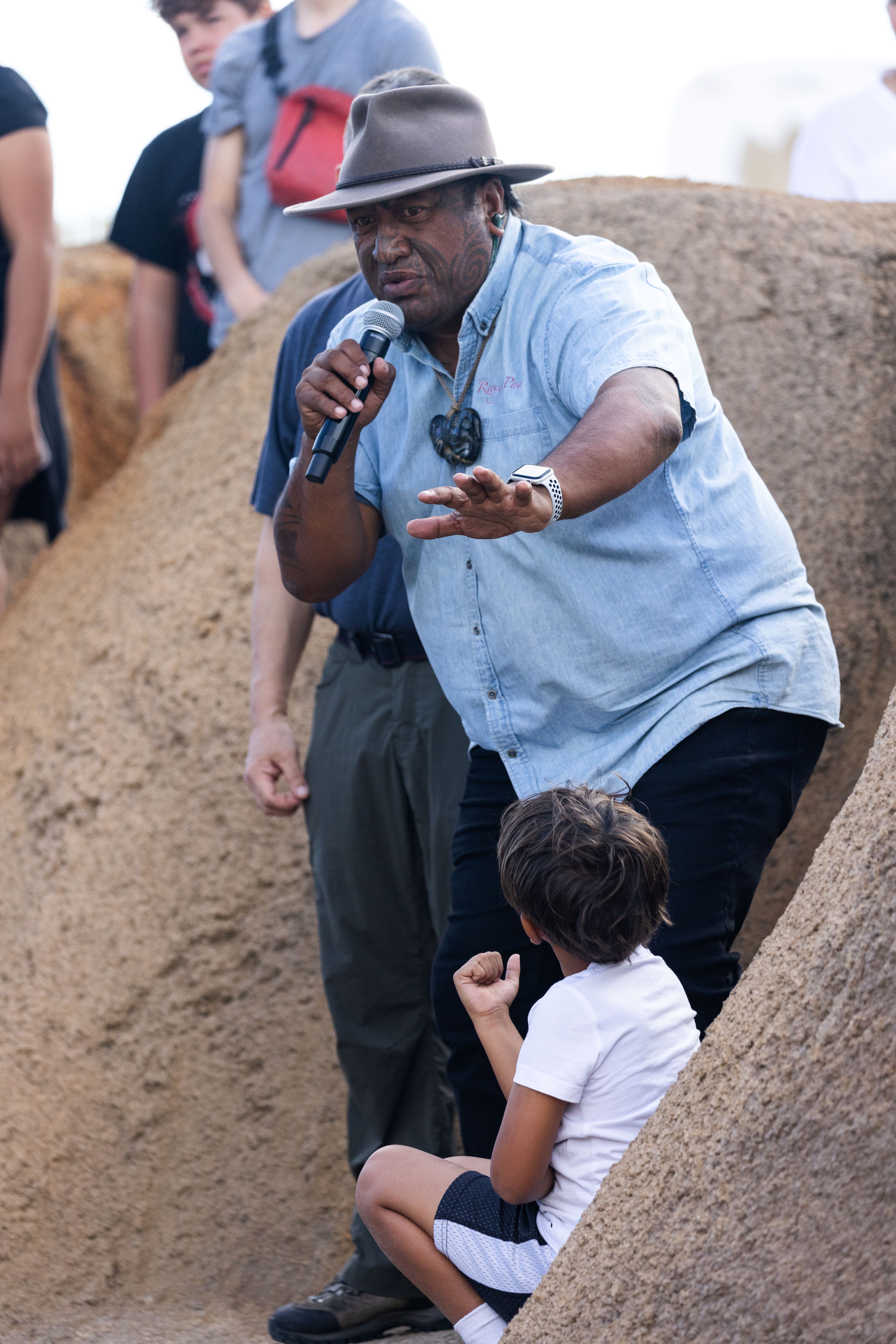 A man speaks using a microphone with a child looking up at him.