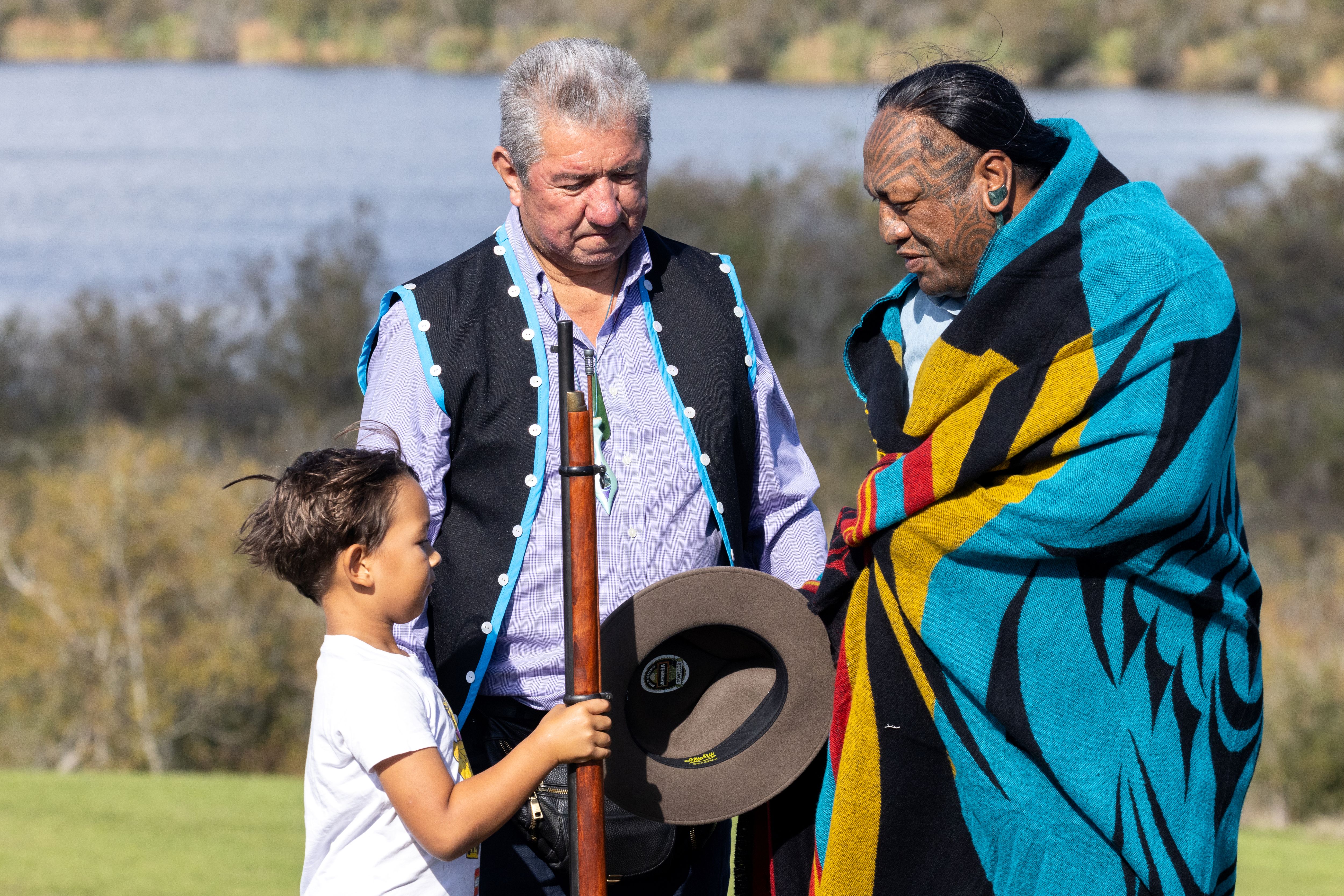 A child hands a person wrapped in a cloth a hat with another person looking on.