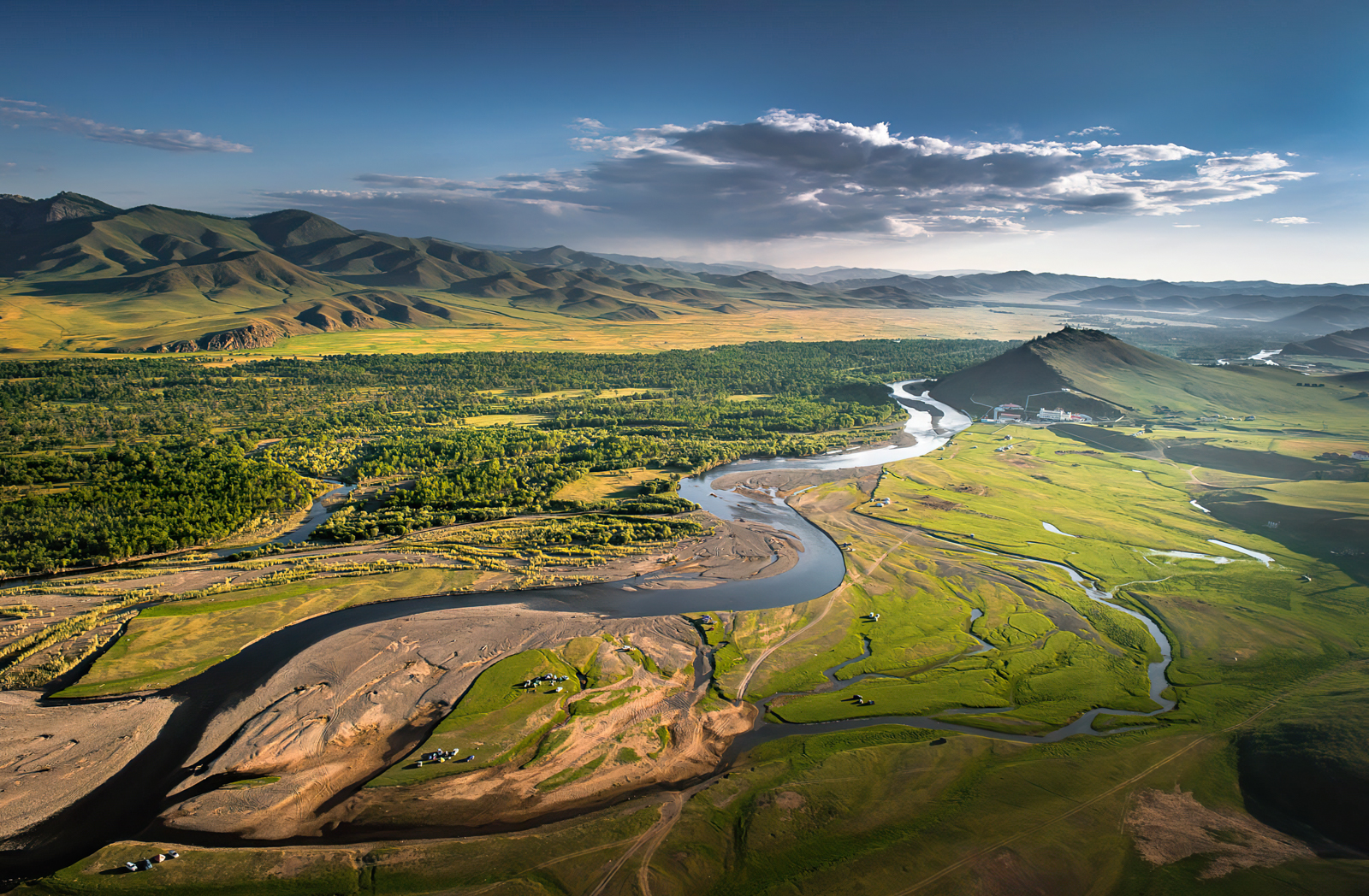 A river meanders through a forested valley with mountains in the background.
