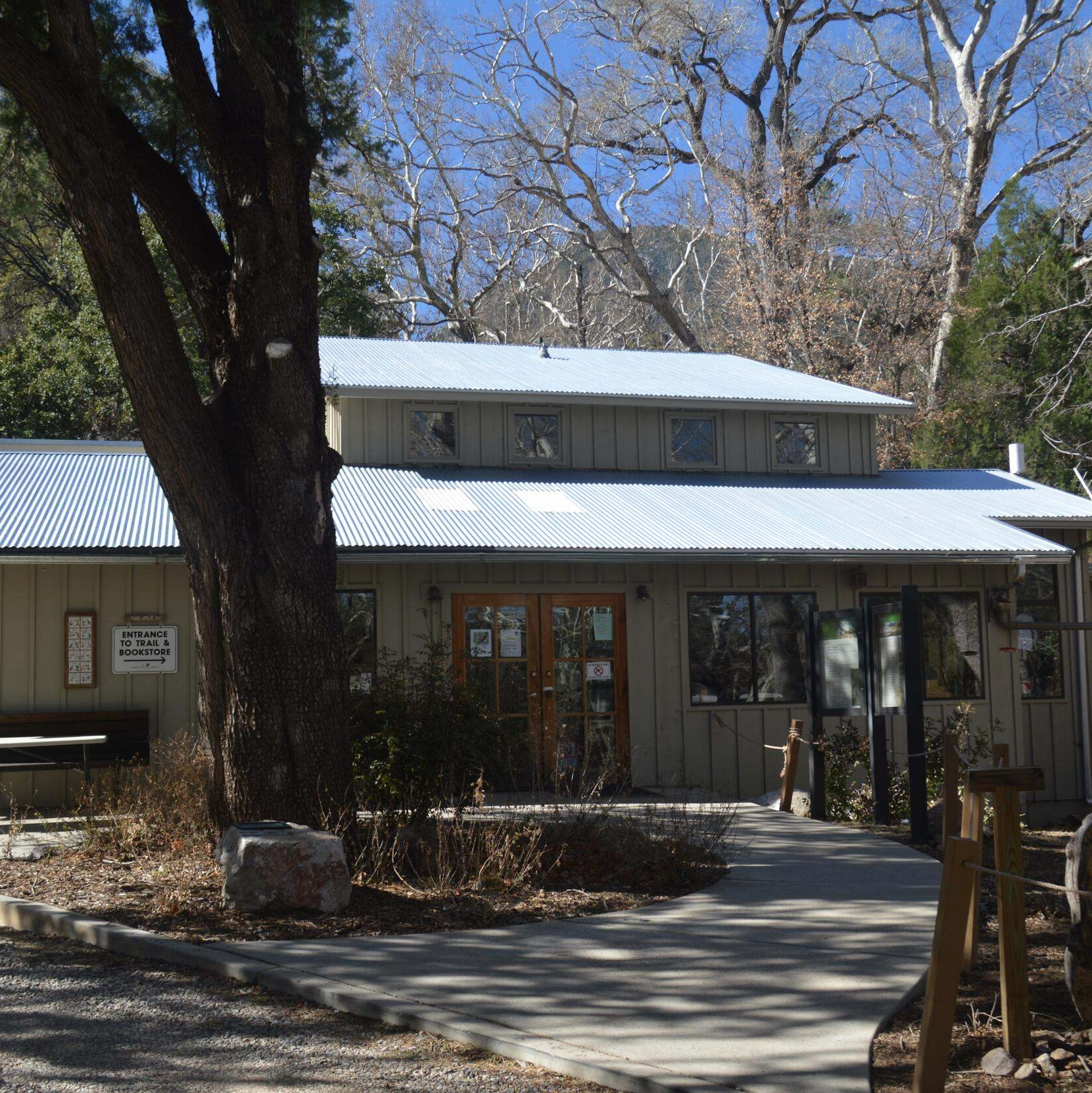 View of the visitor center building with a large tree in front and smaller trees behind it.