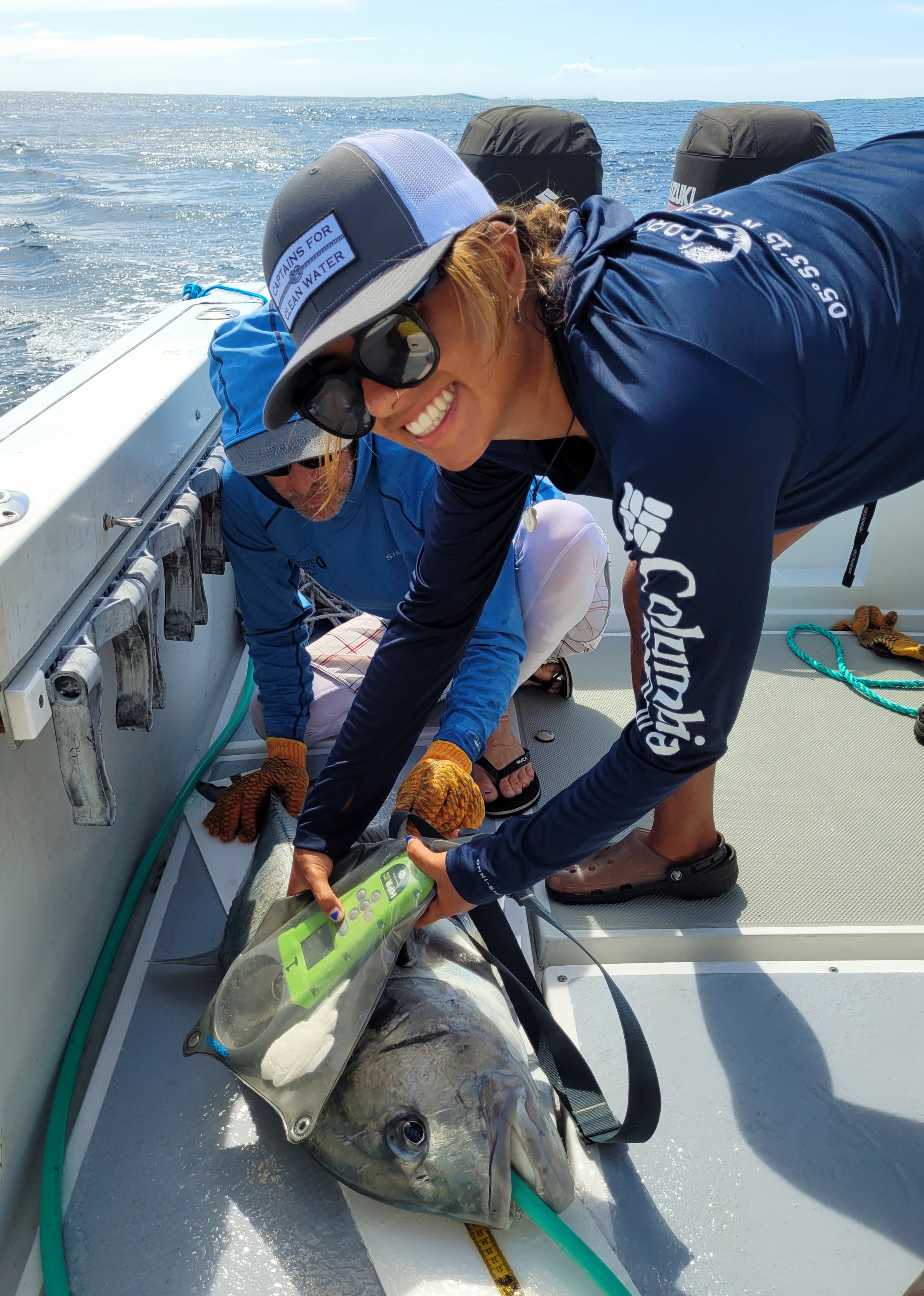 Two volunteers scan a fish on the deck of a boat.