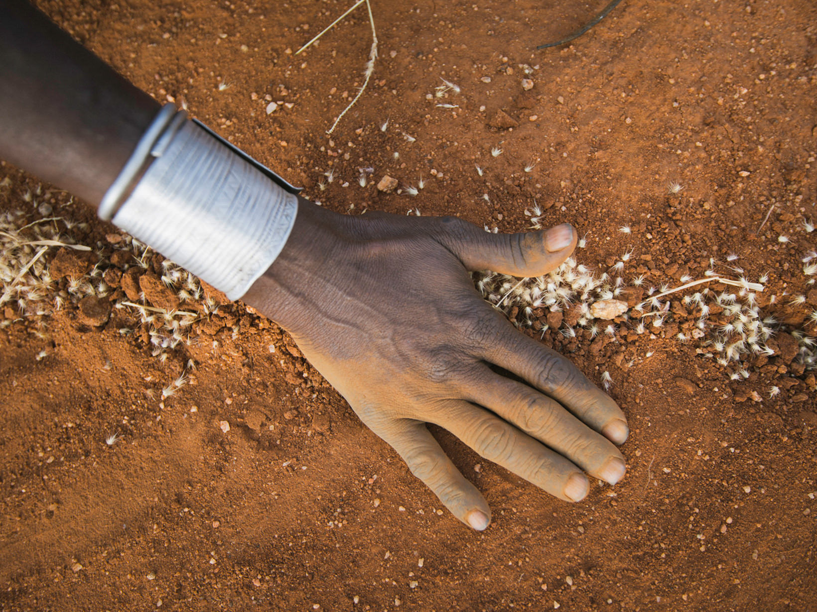 A hand stretches out and touches red dirt.
