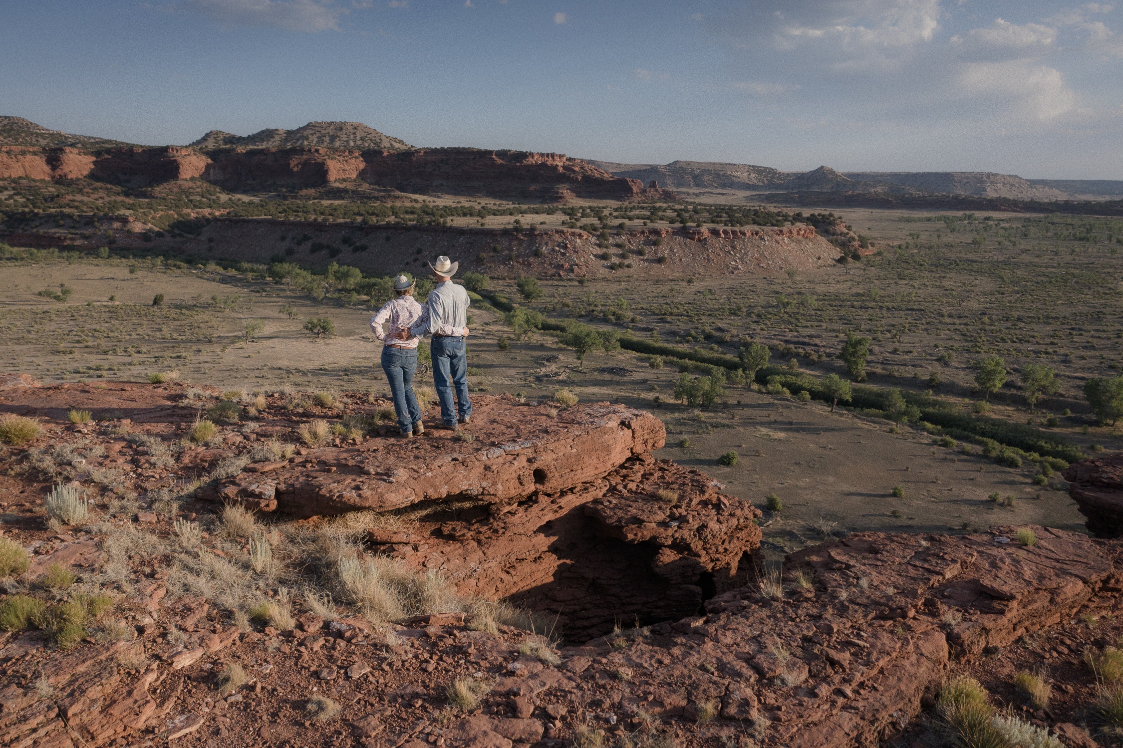 A man and a woman stand on the edge of a rocky red canyon.