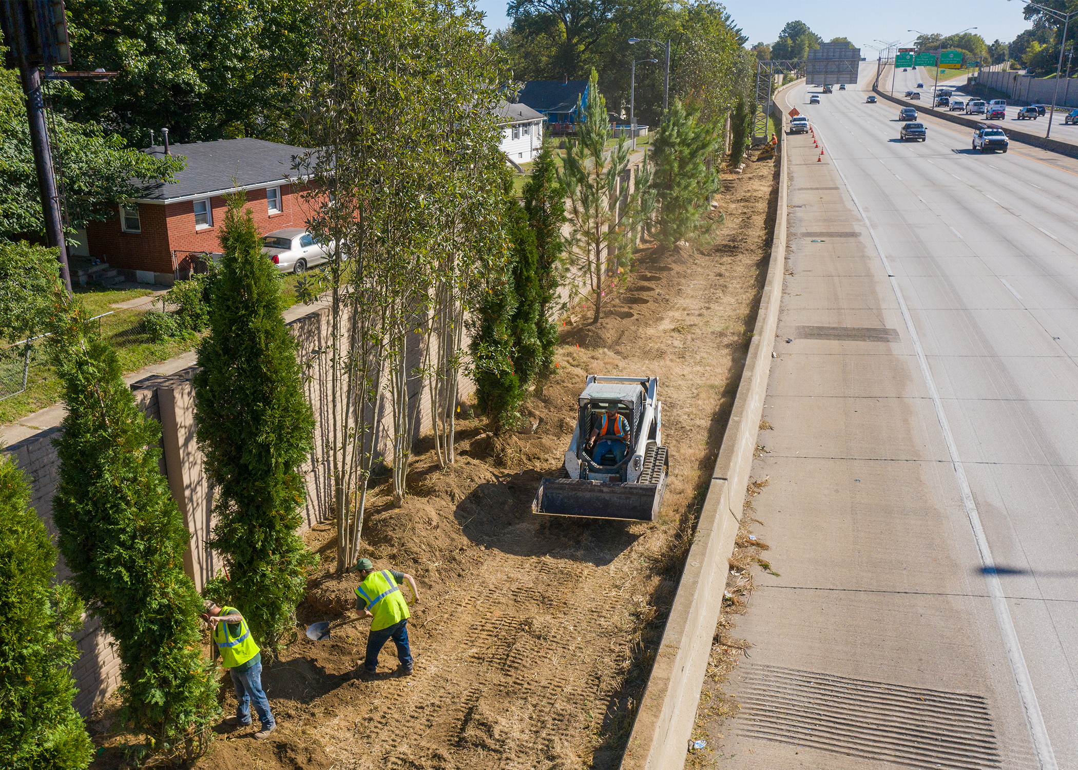 Teams work with shovel in hand and heavy machinery to help plant trees along the Waterson Expressway in Louisville.