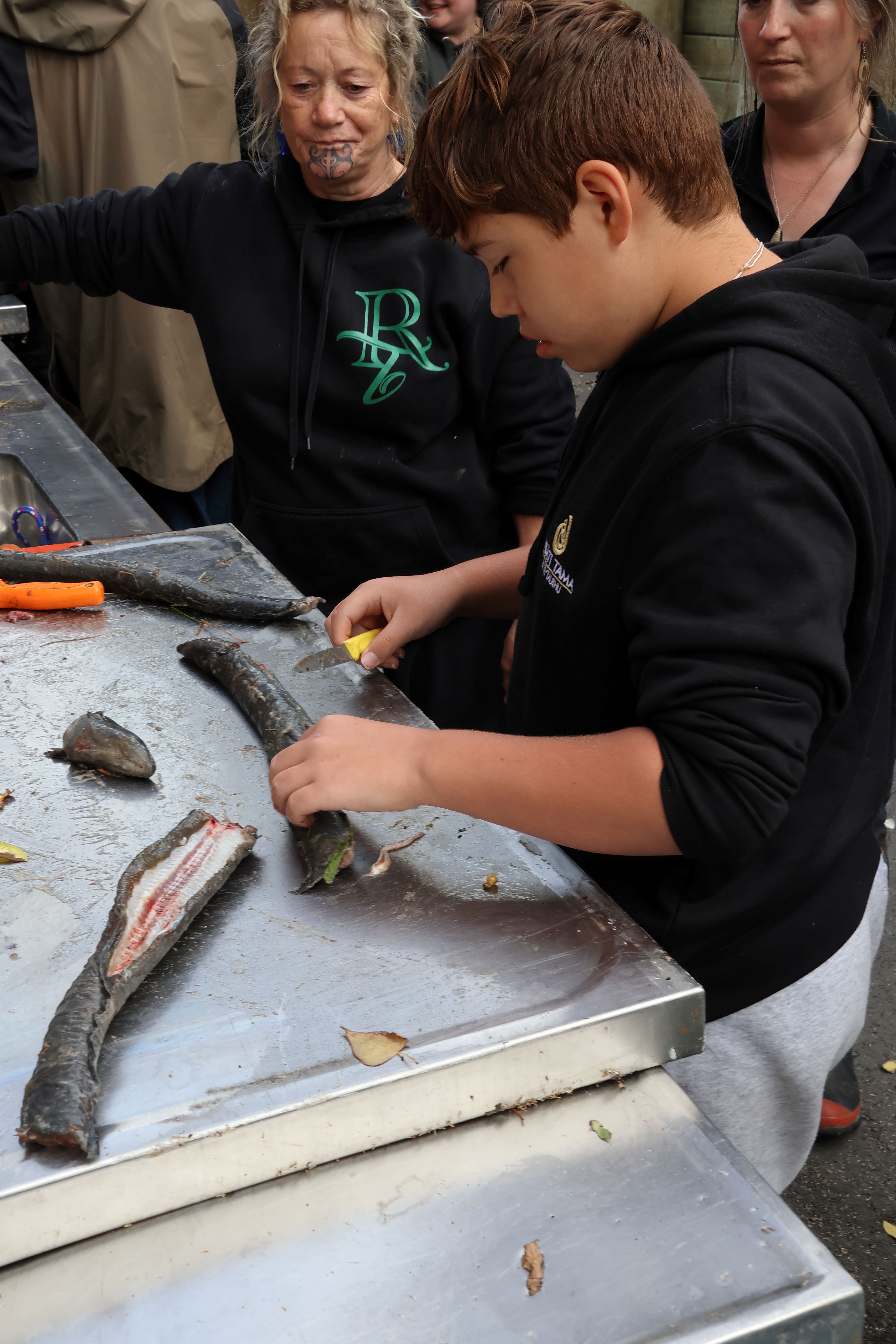 A young person filets fish with an adult supervising.