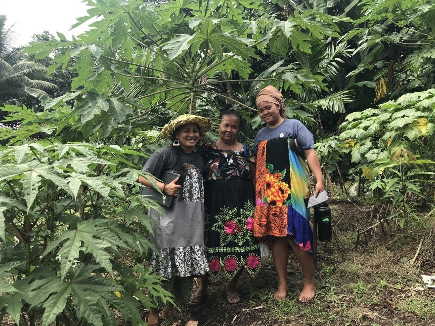 Three women pose together under green foliage.