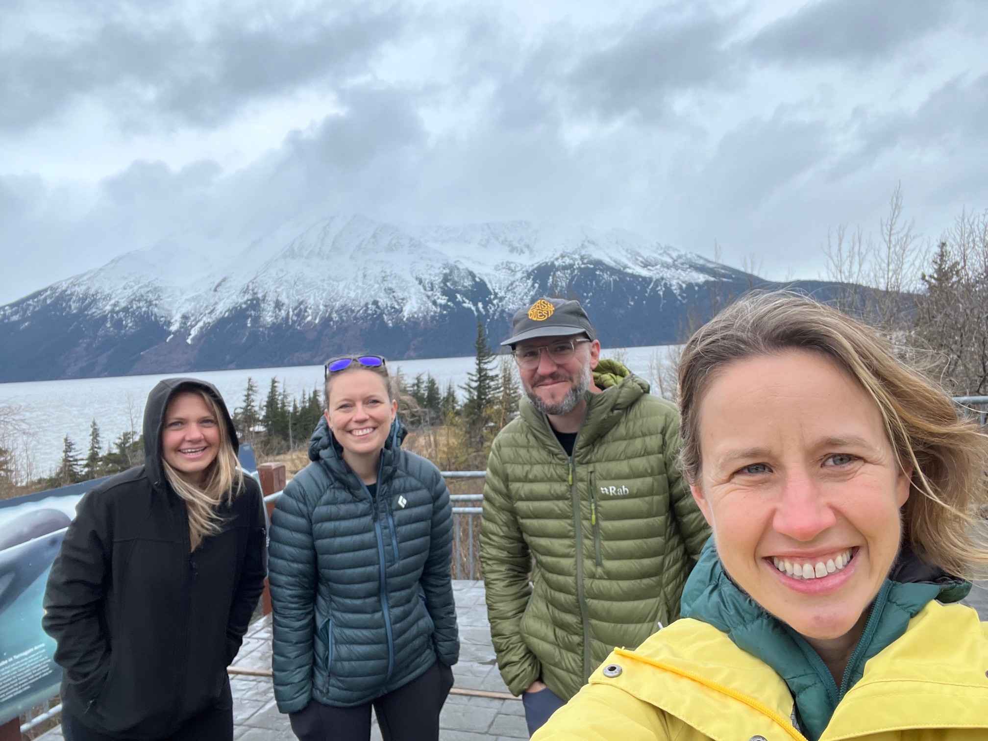 Snowcapped mountains serve as the backdrop for four people posing for a picture.