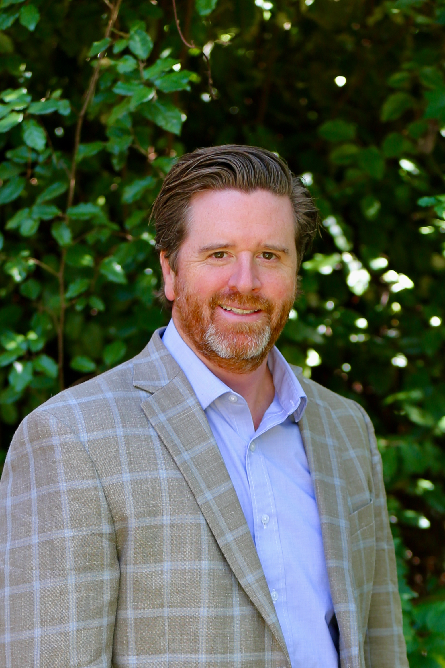 A man wearing a blue shirt and sport coat poses for the camera.