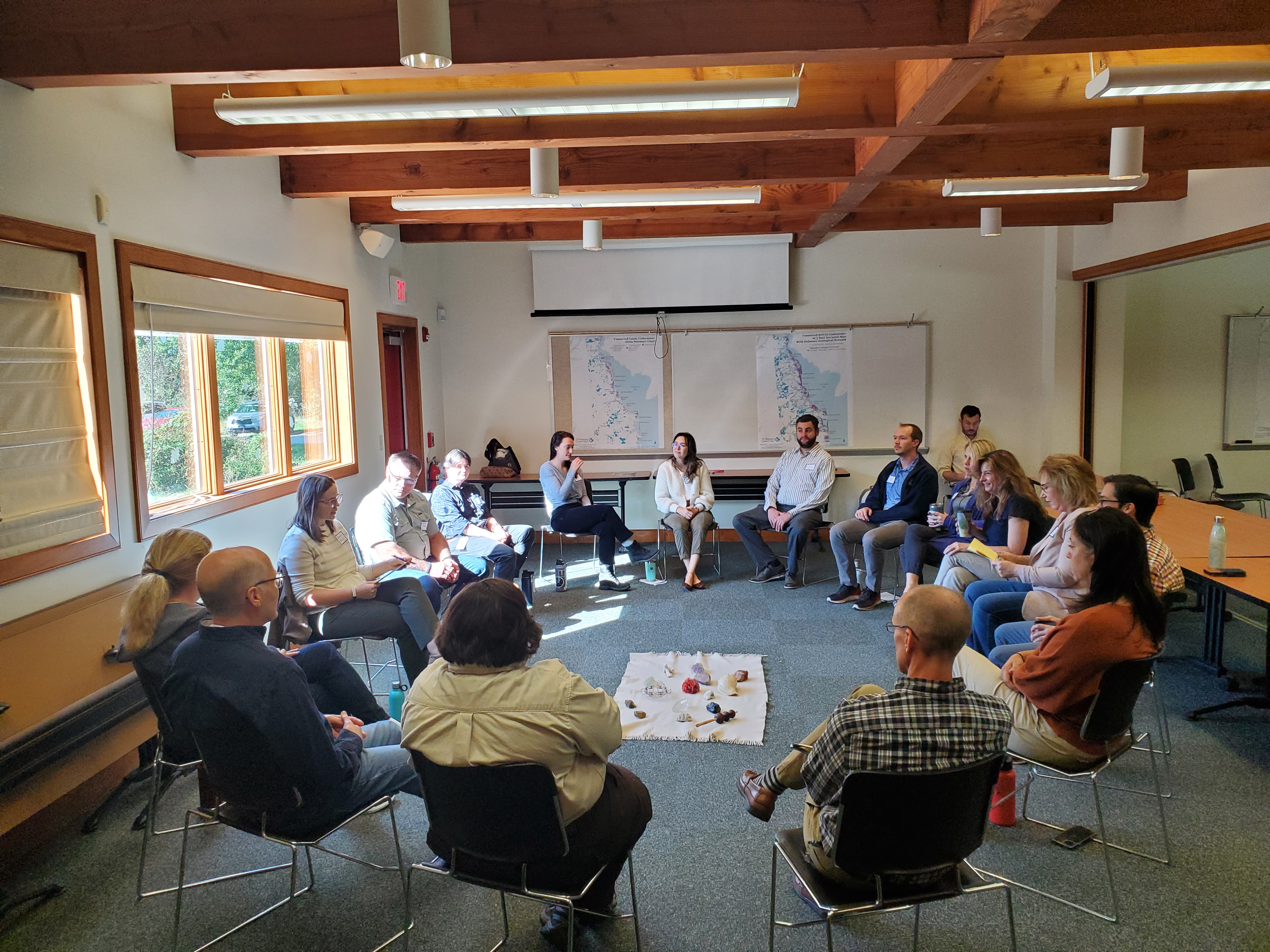A group of people sit in chairs in a circle facing each other. 