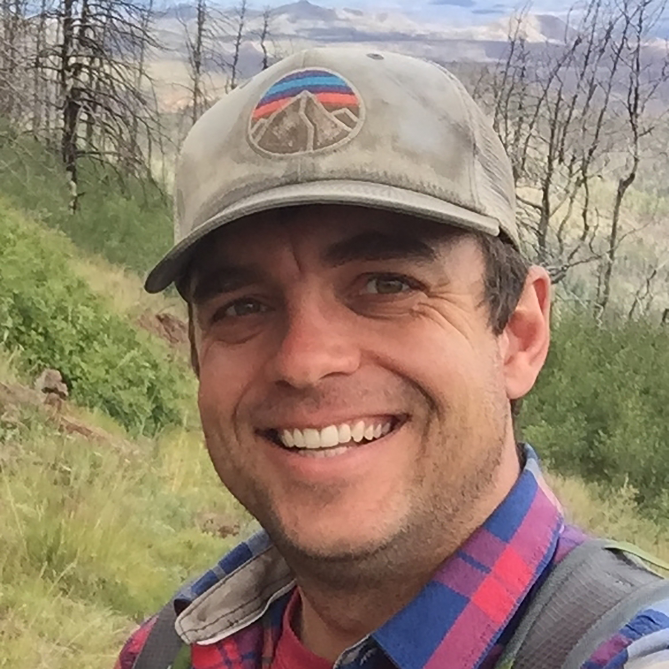 Smiling man wearing cap and flannel shirt.