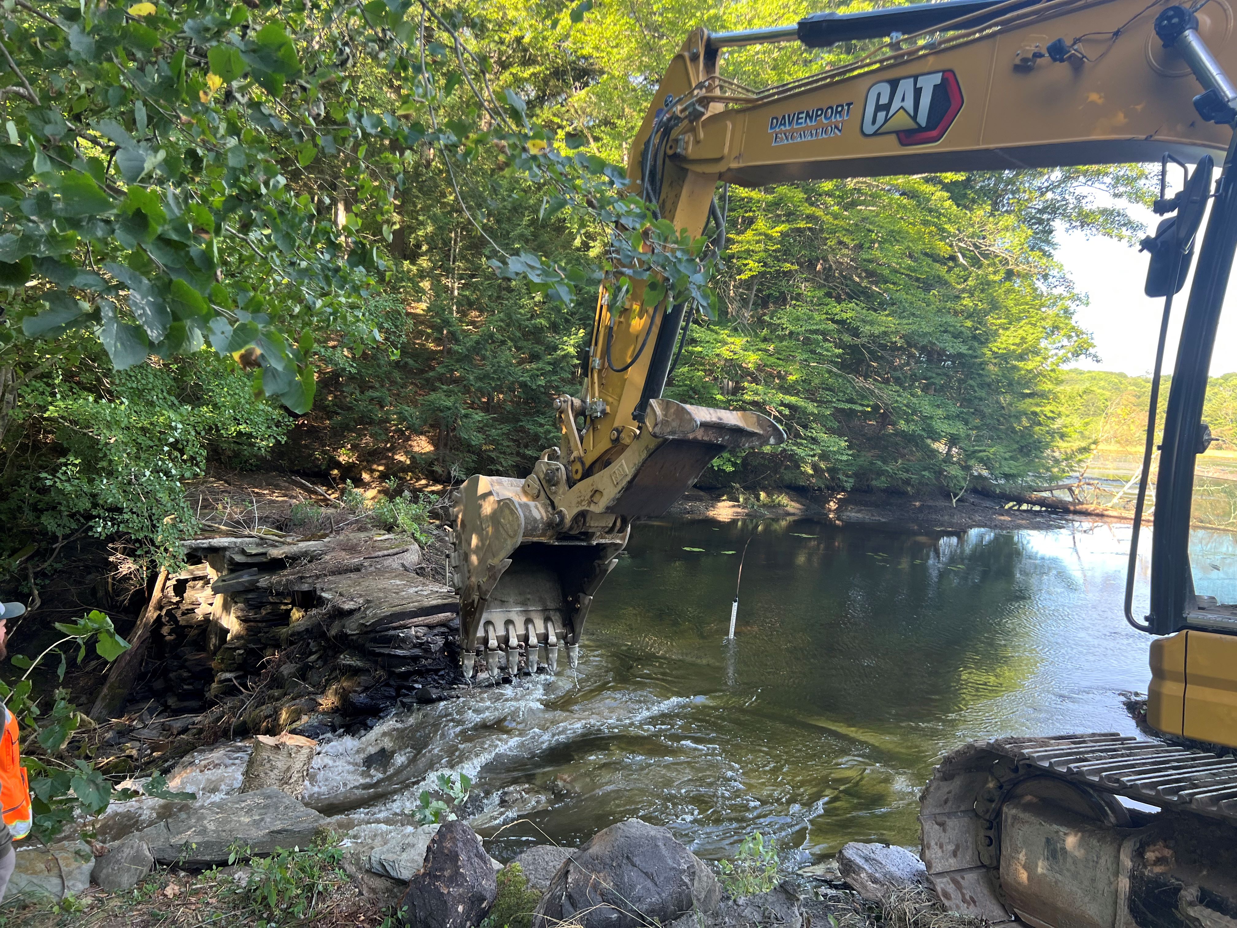 A backhoe removes material to open a small dam.