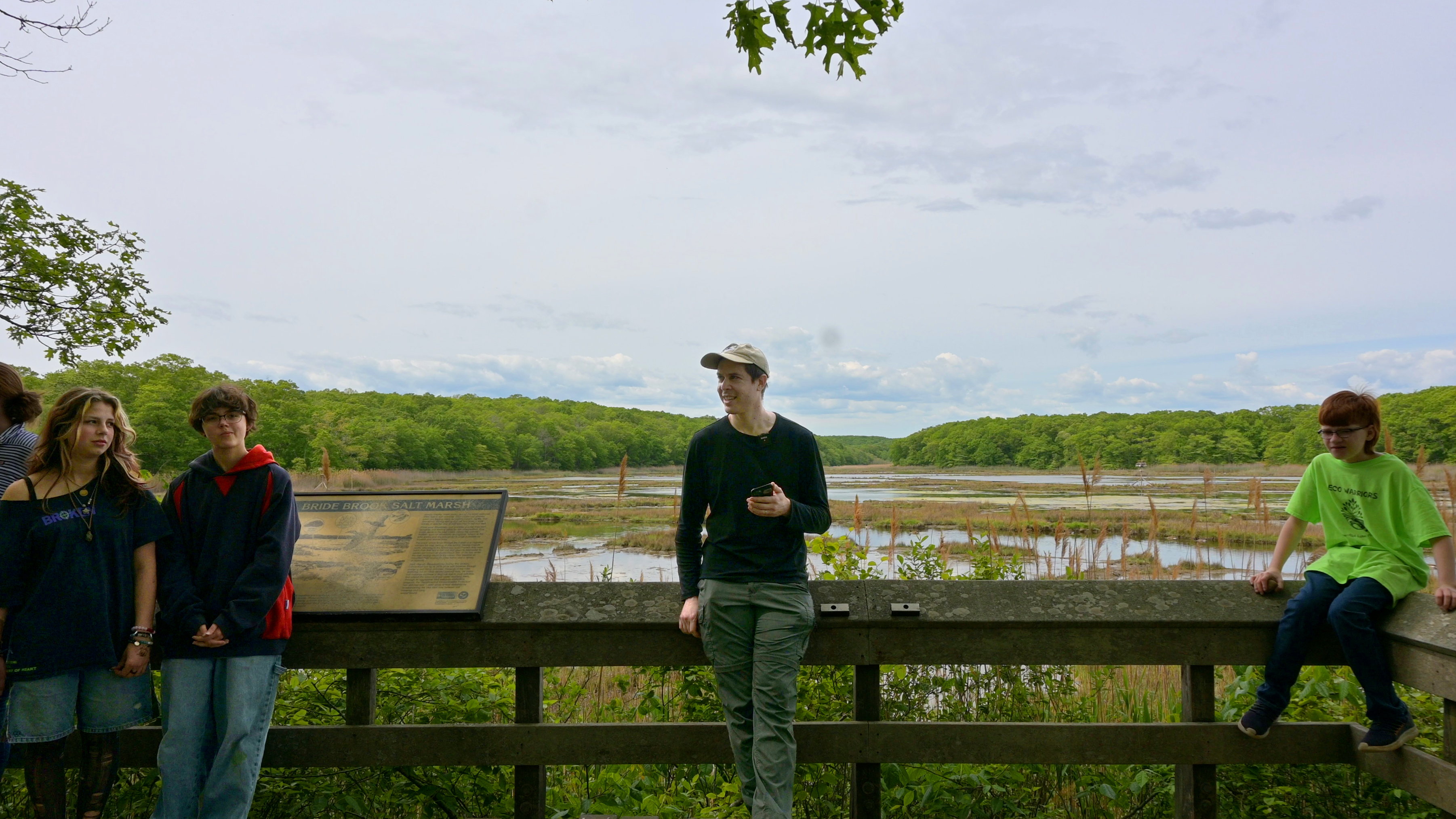 Four individuals standing at a wooden observation deck overlooking a scenic wetland area.