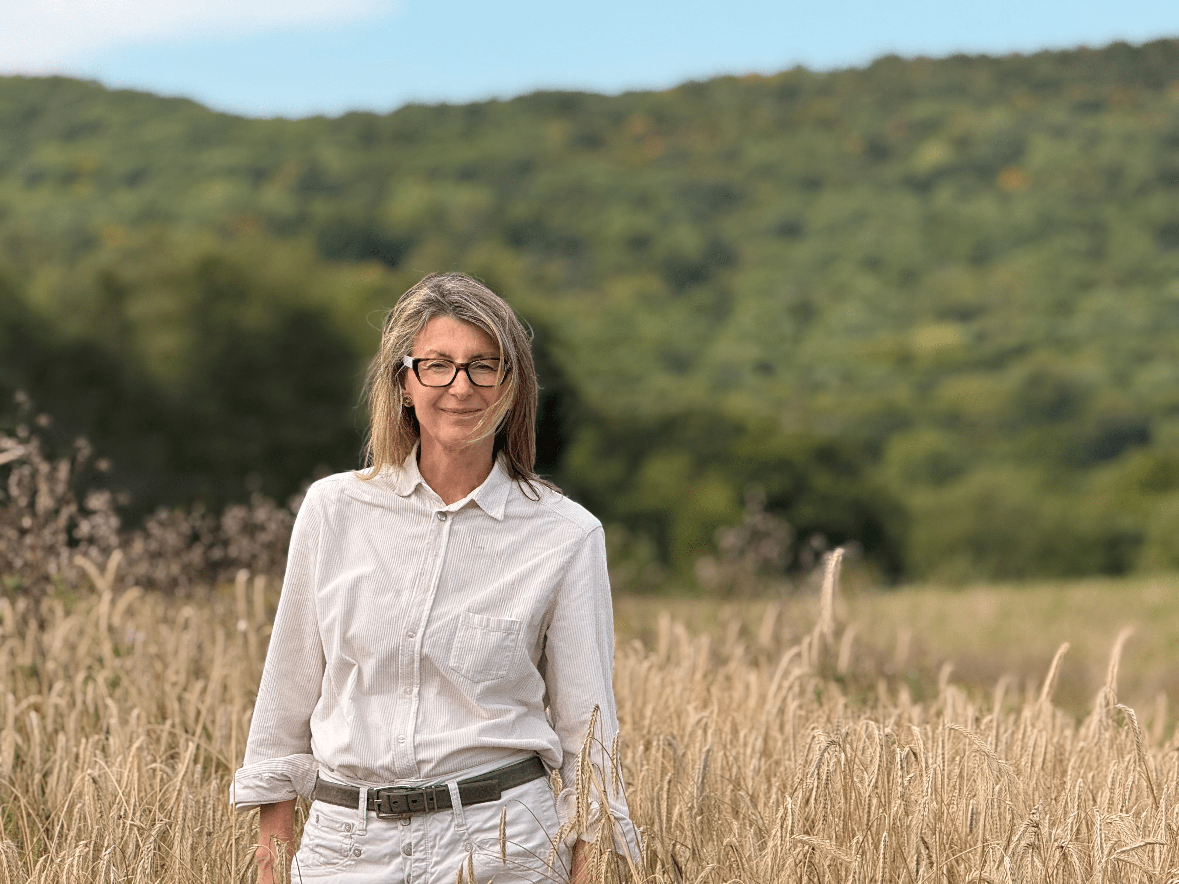 A woman wearing glasses stands in a grassy field. 