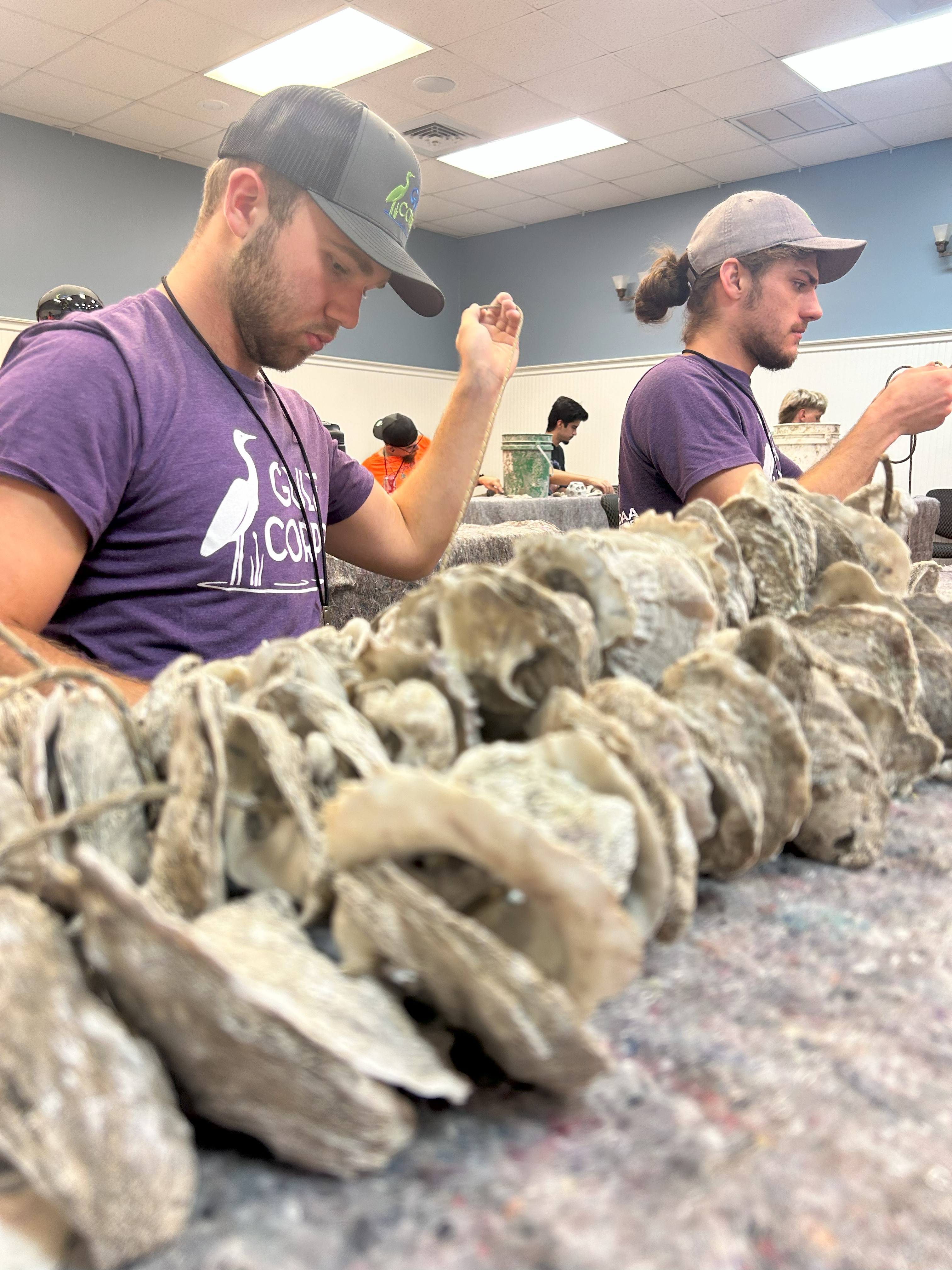 Two men wearing hats use their hands to work with material.