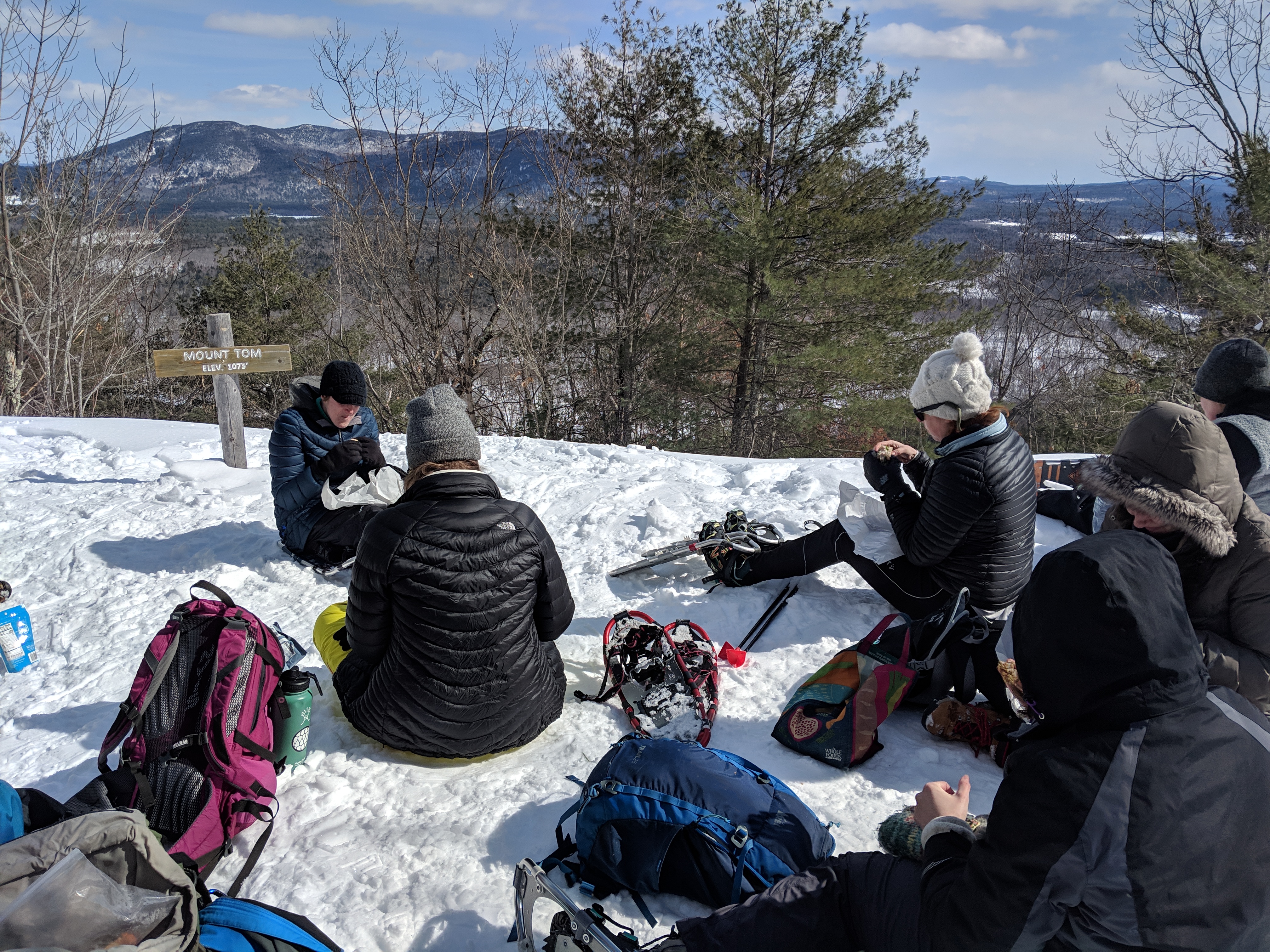 A group of people wearing winter gear sit and rest in view of a mountain.