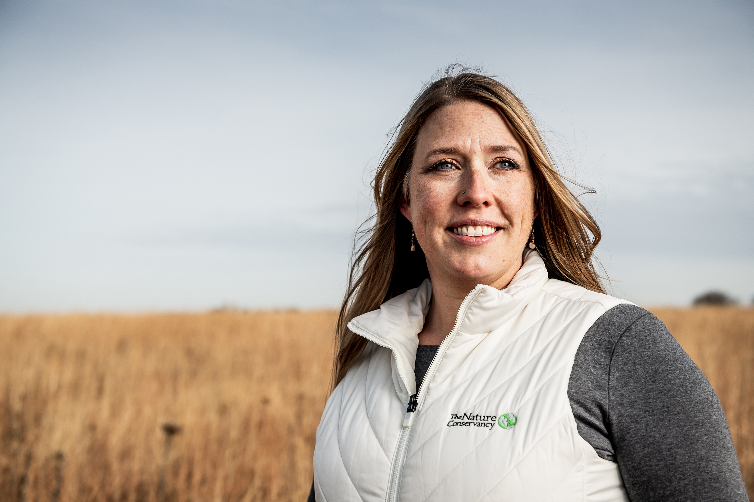 Looking away from the camera, Dr. Heidi Mehl stands, smiling, in a prairie. 