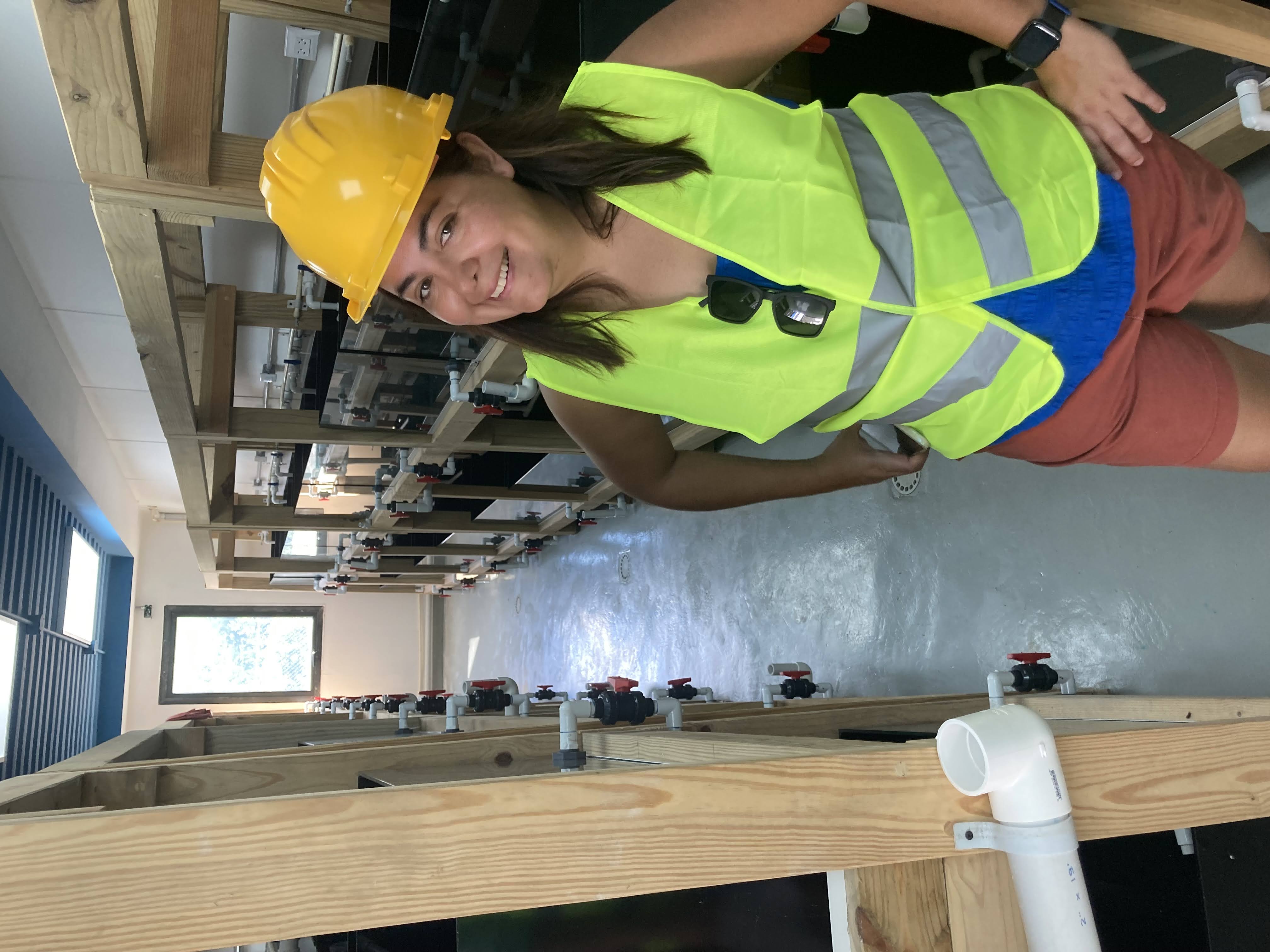 A woman in a yellow safety vest and helmet smiles at the camera.
