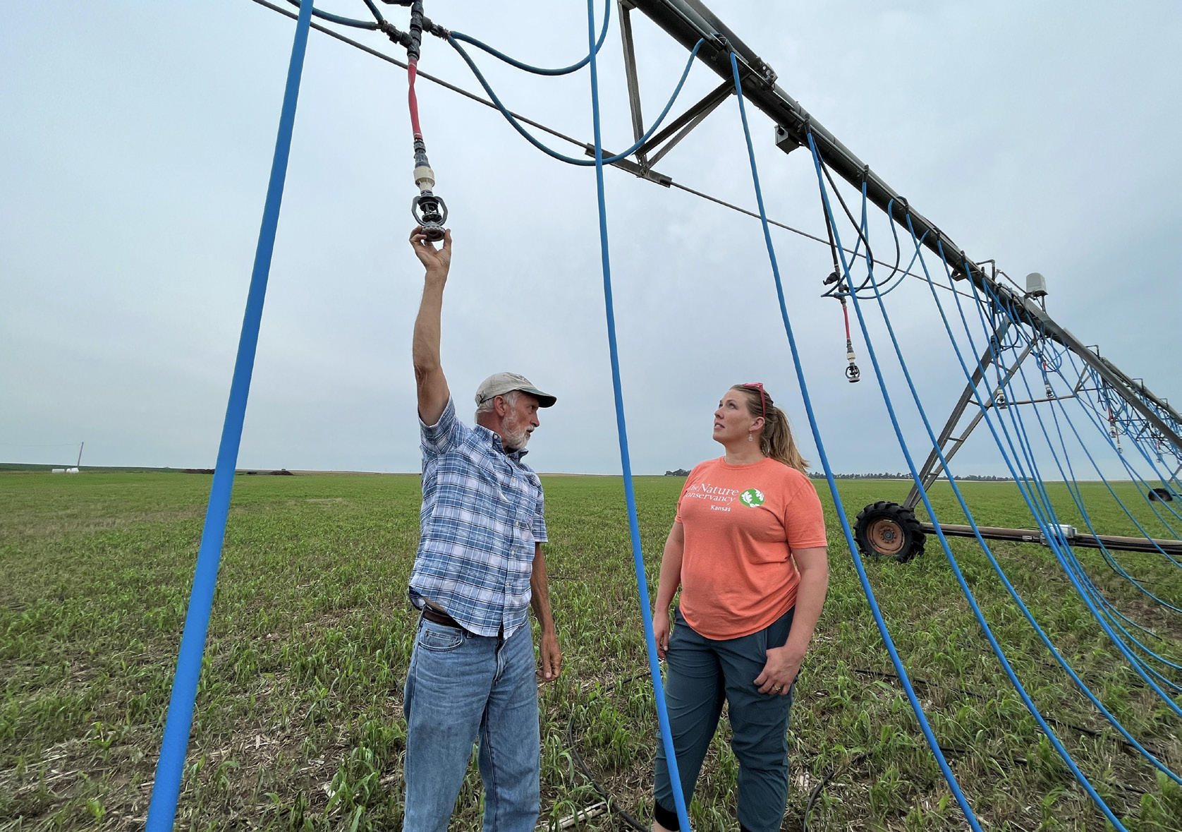 Two people stand underneath an irrigation system in a farm field.