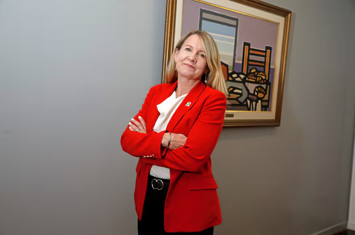 Jennifer Morris, CEO de The  Nature Conservancy, posa con una chaqueta roja, blusa blanca, pantalón negro y brazos cruzados en una oficina de muros gris con un cuadro de fondo.