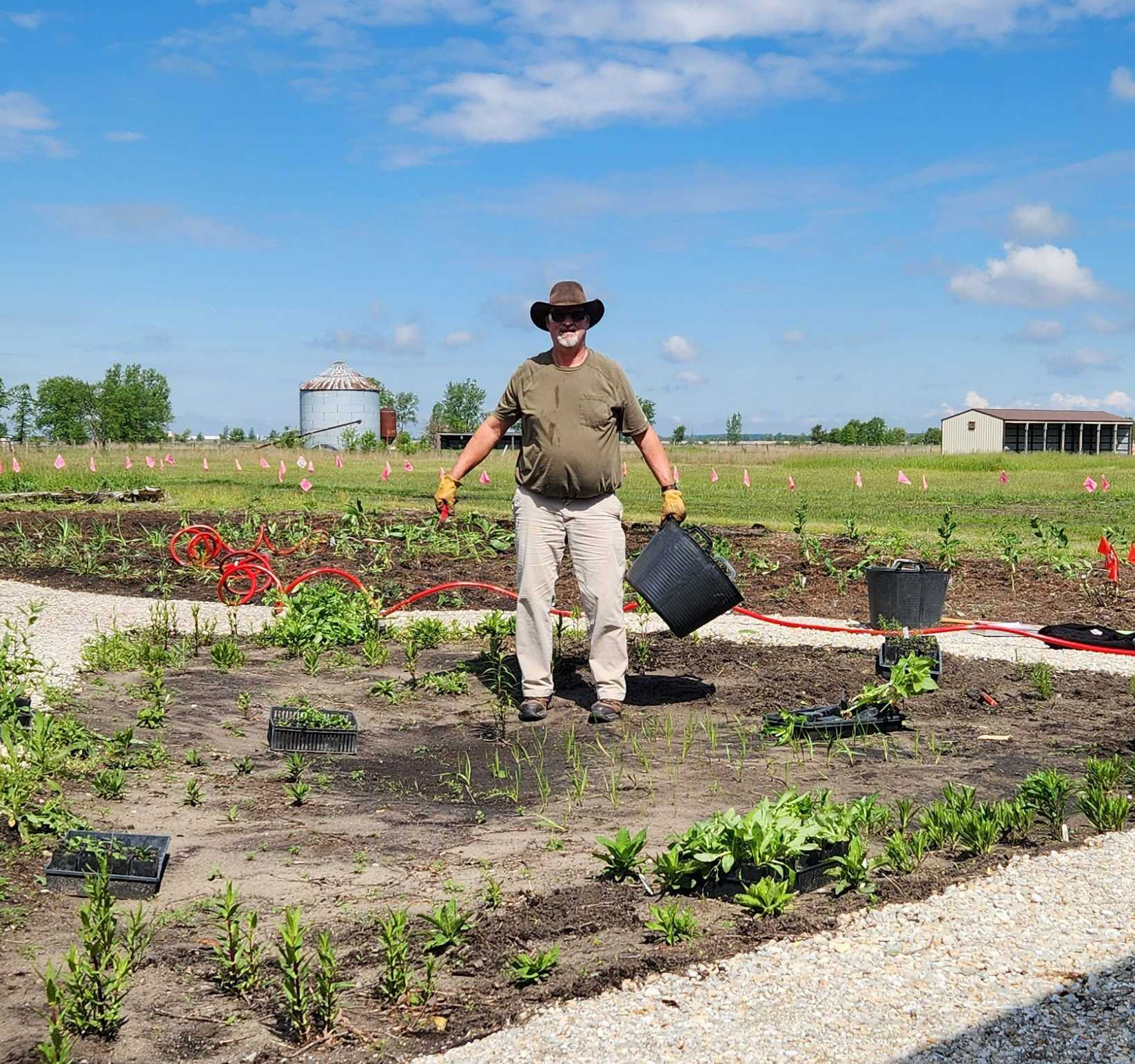 A man wearing a hat poses for a photo in a garden.