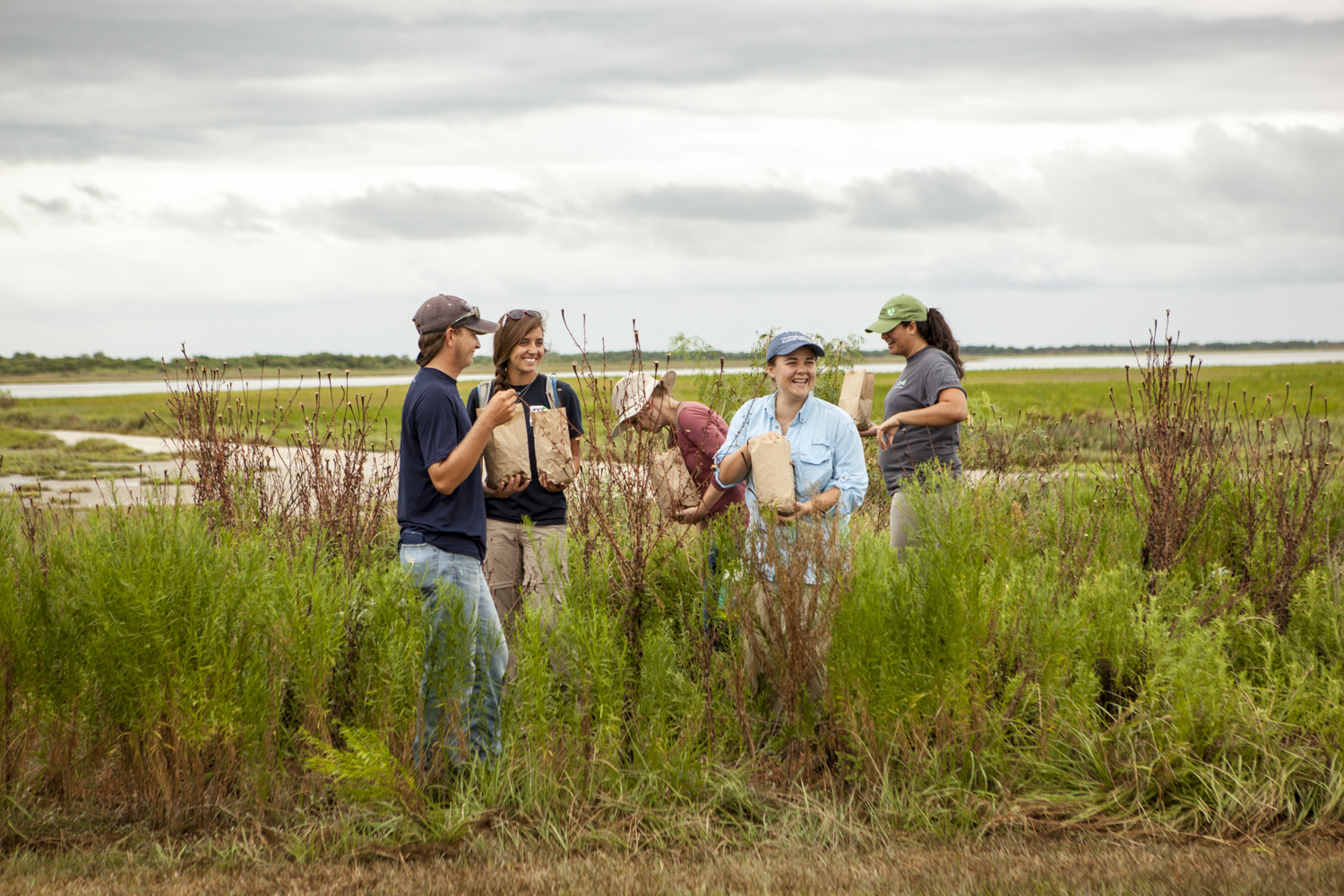 A group of men and women spread seeds from a brown bag.