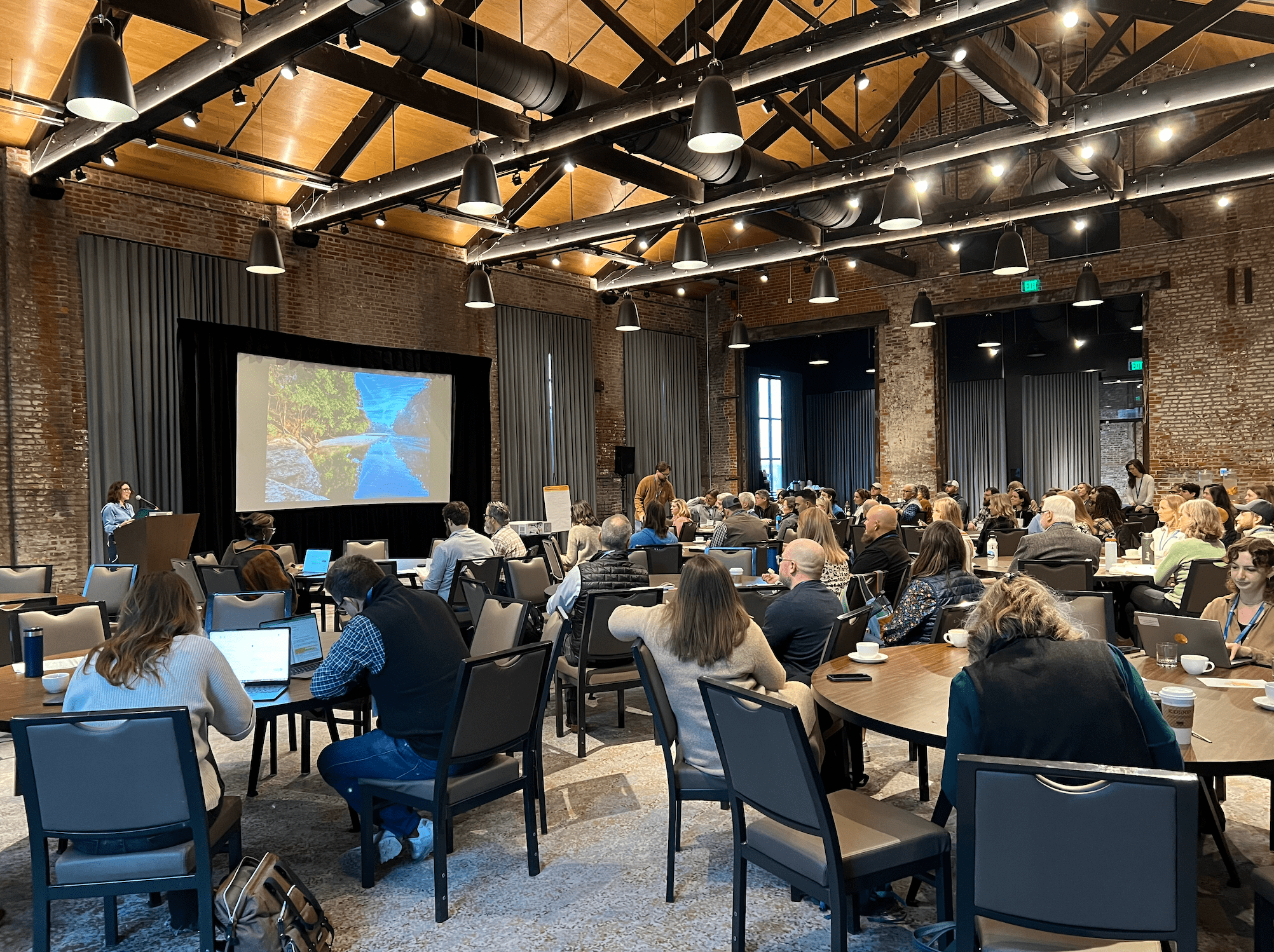 People gather around tables to listen to a presenter.