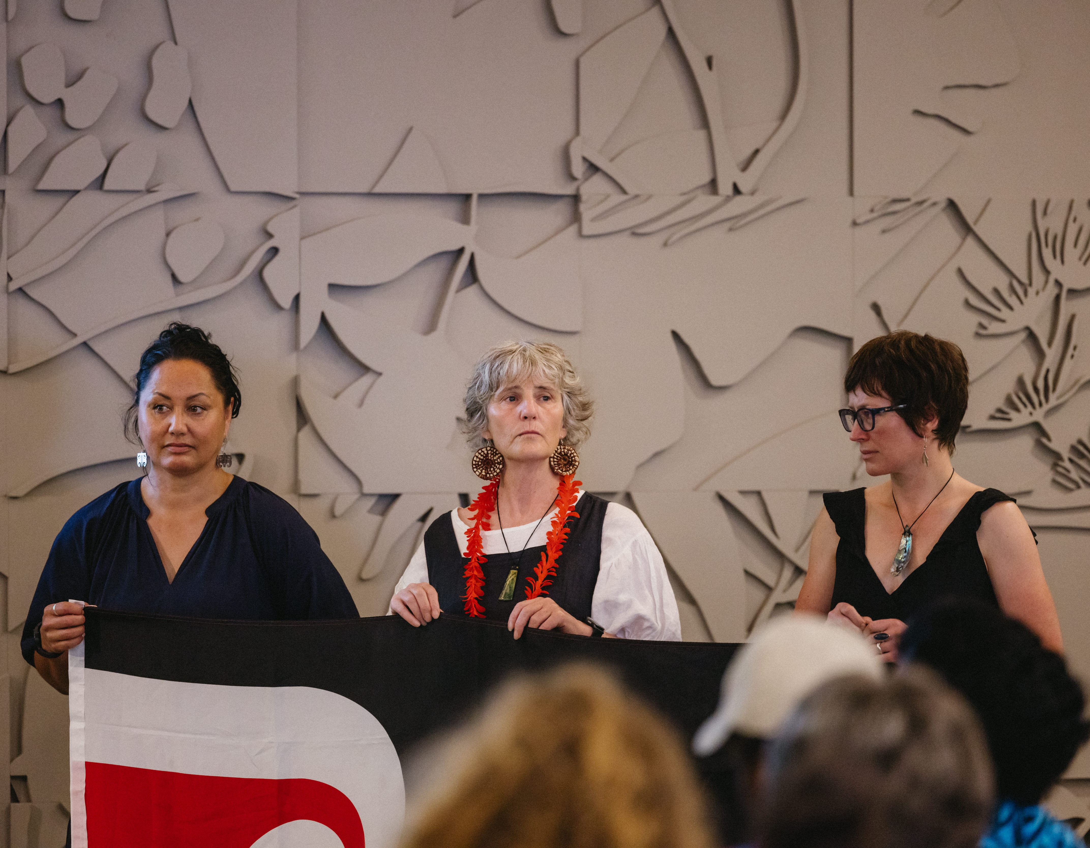 Three women stand together and hold a flag.