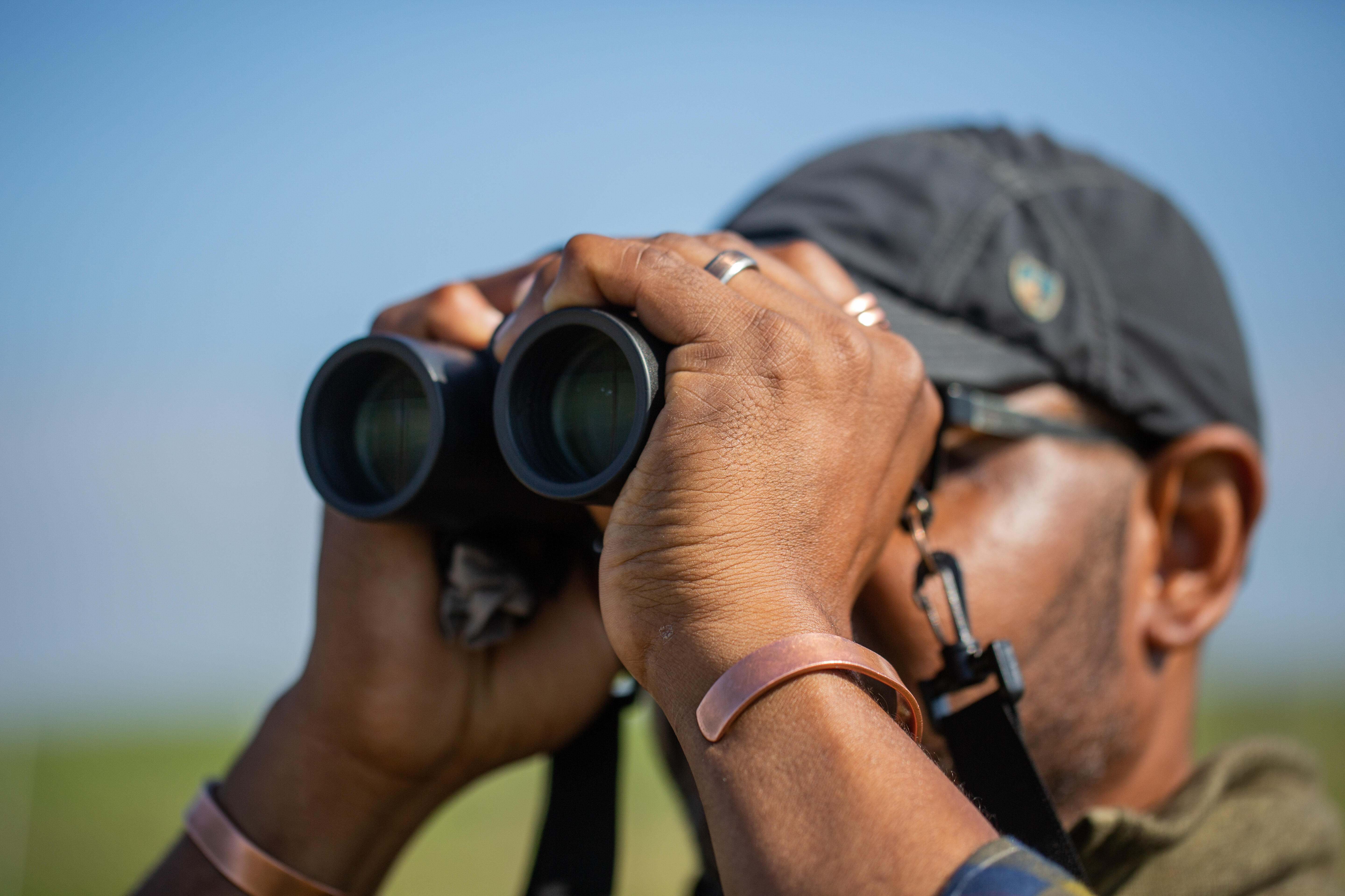 A man looks through binoculars to watch birds. 