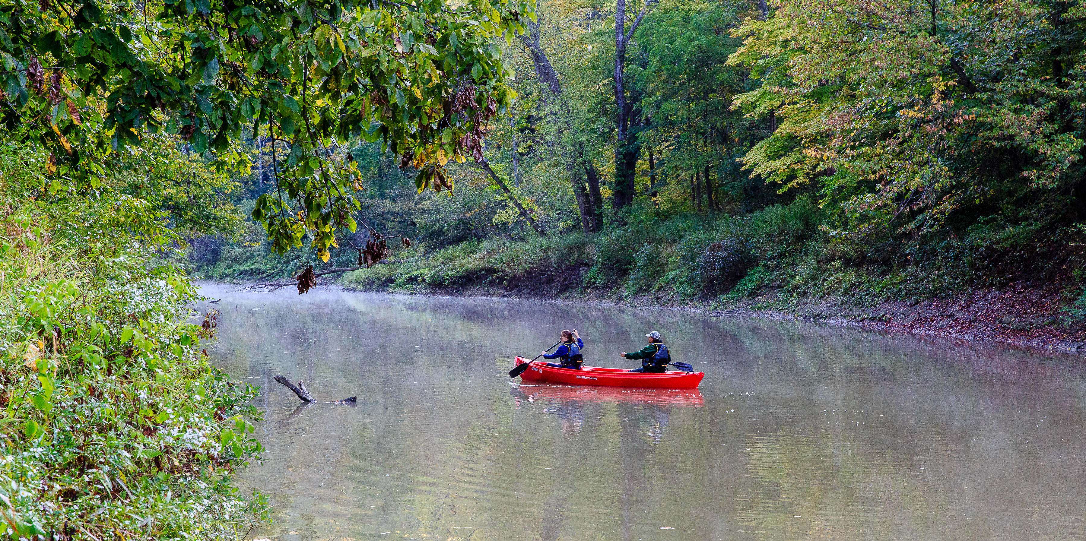 Two people paddle on a river in a red kayak.