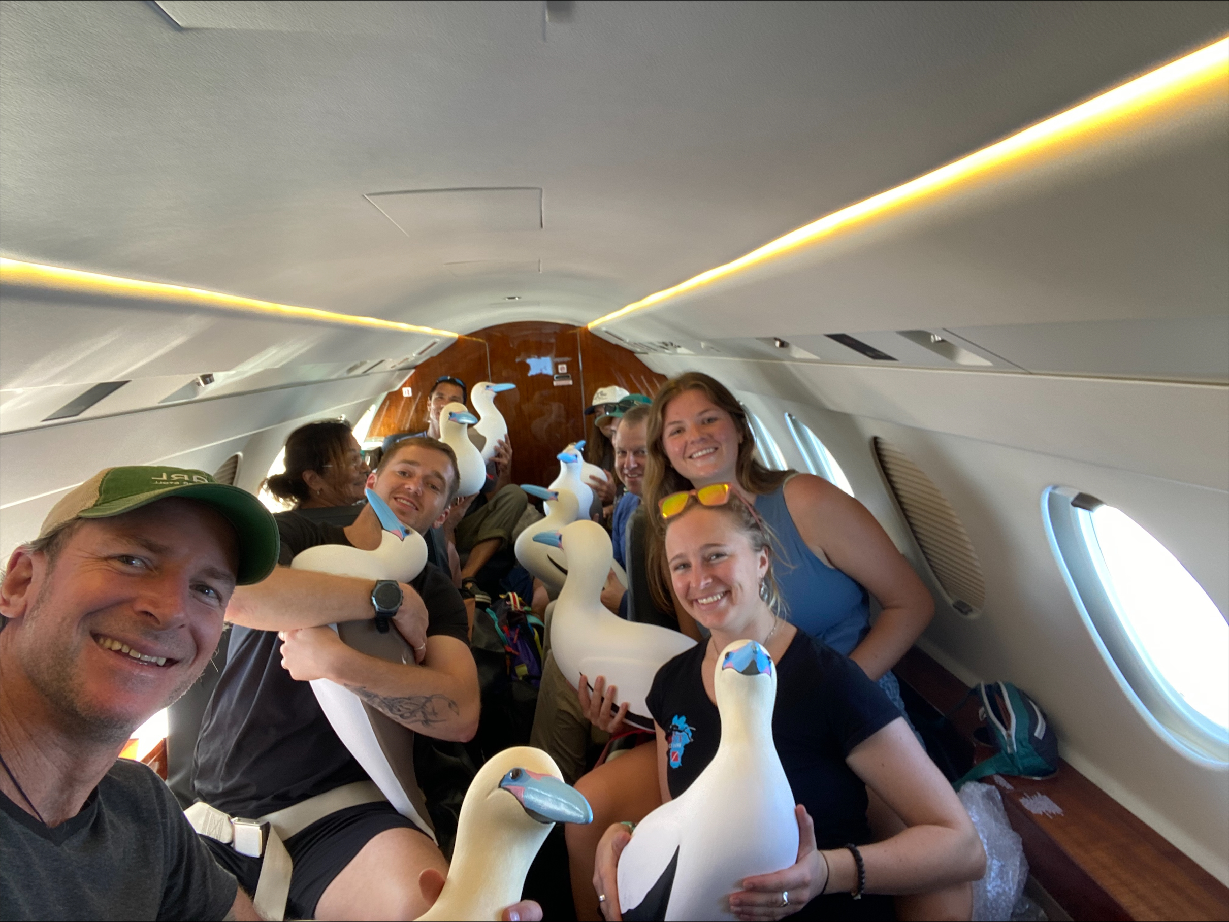 A group of young people on a plane hold bird decoys and smile.