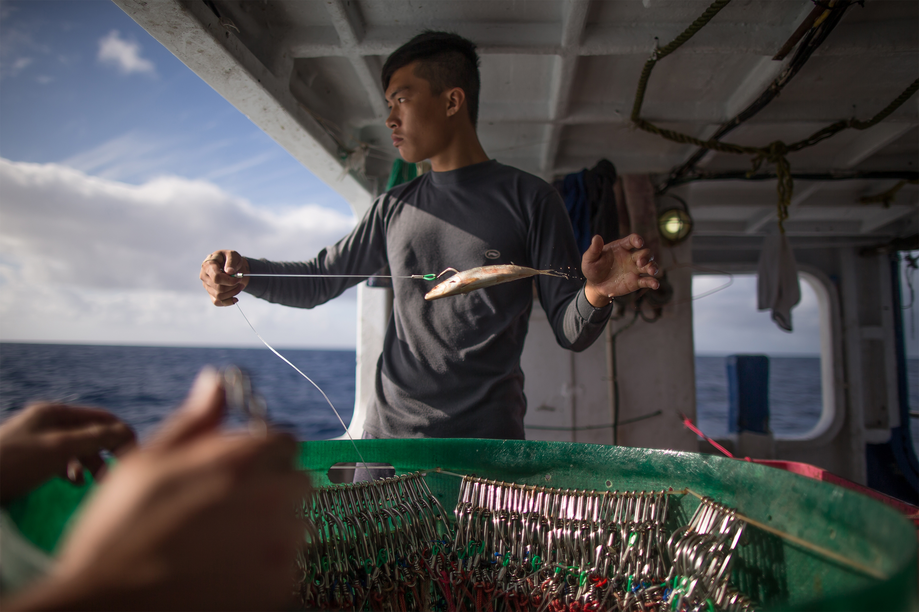 A man stands on the deck of a boat and holds a fishing line with a fish on it.