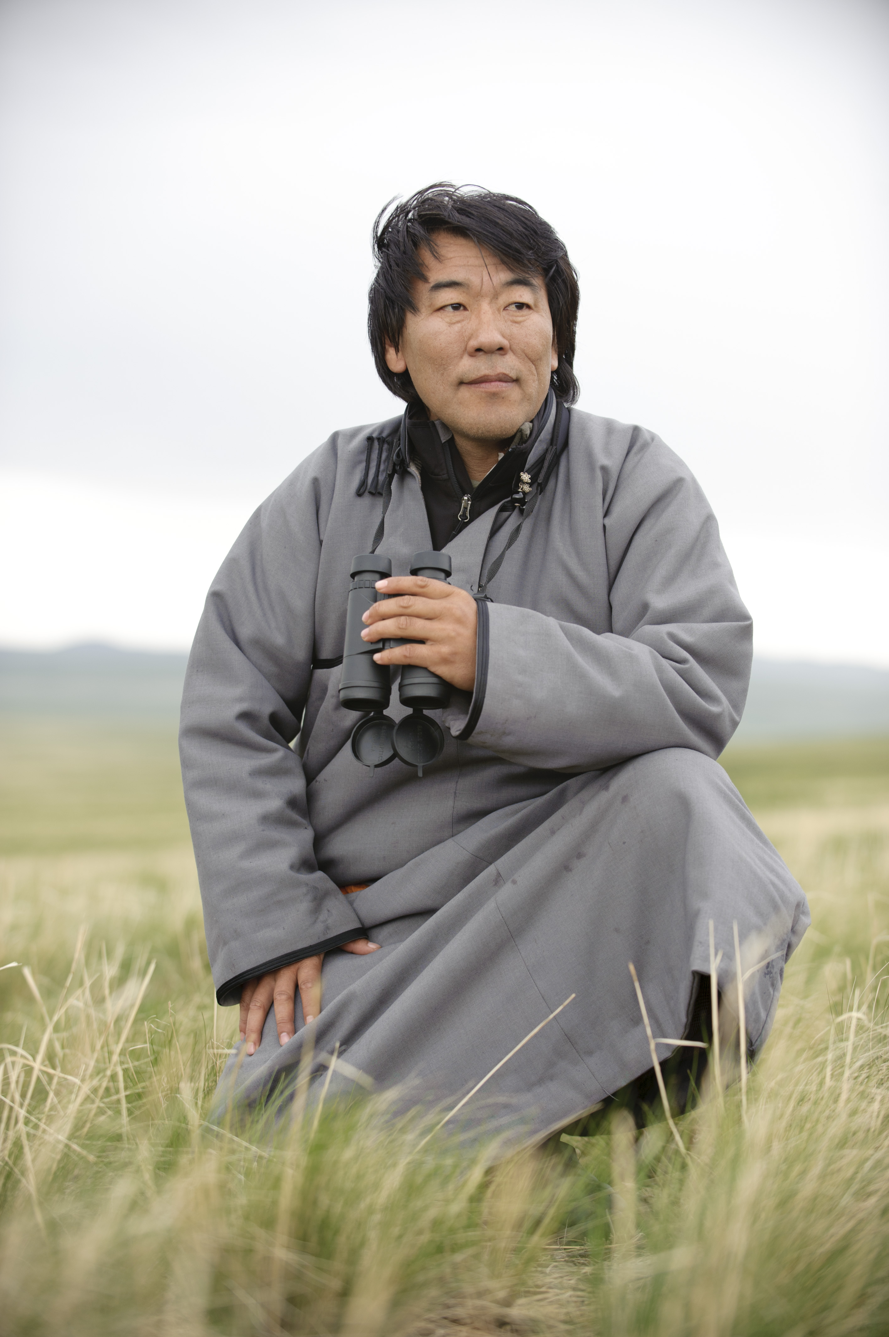 A man wearing a gray coat stands in a grassy field.