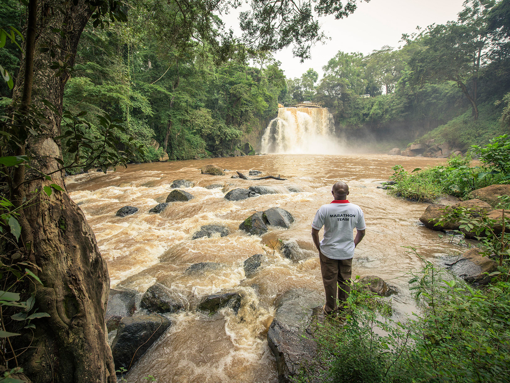 a man with his back to camera looks at a muddy river