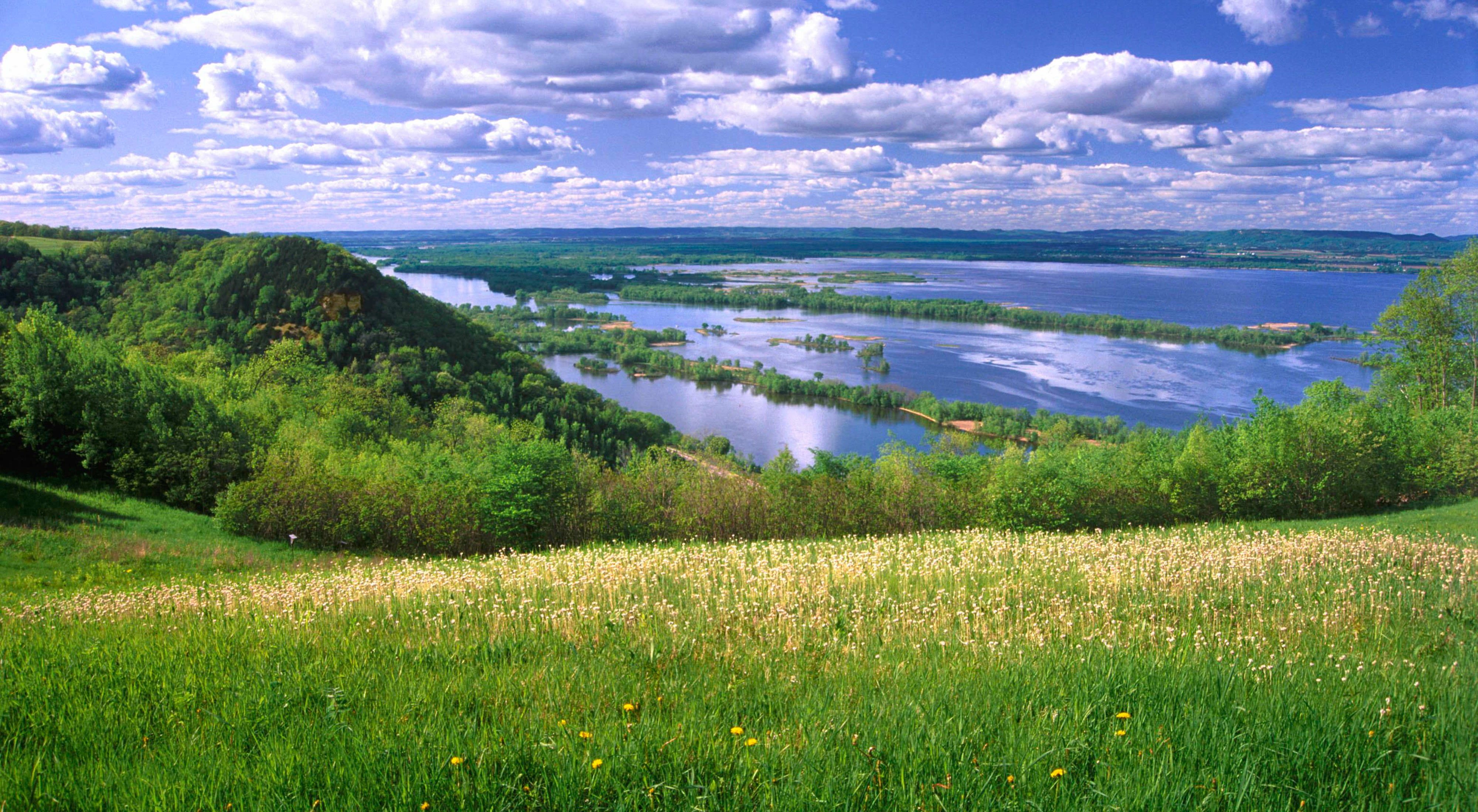 Grass field overlooking blue water under cloudy skies.