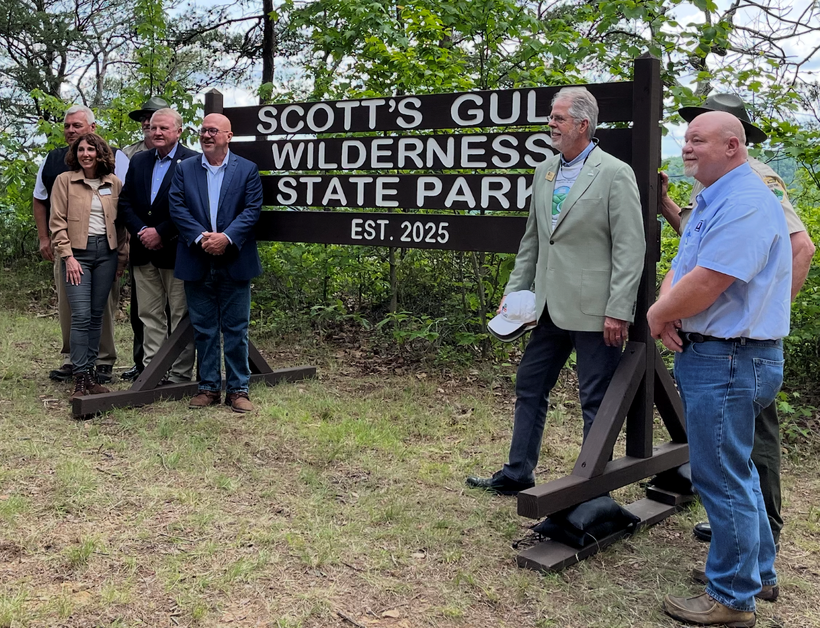 A group of six people gather around a sign to pose for a picture.