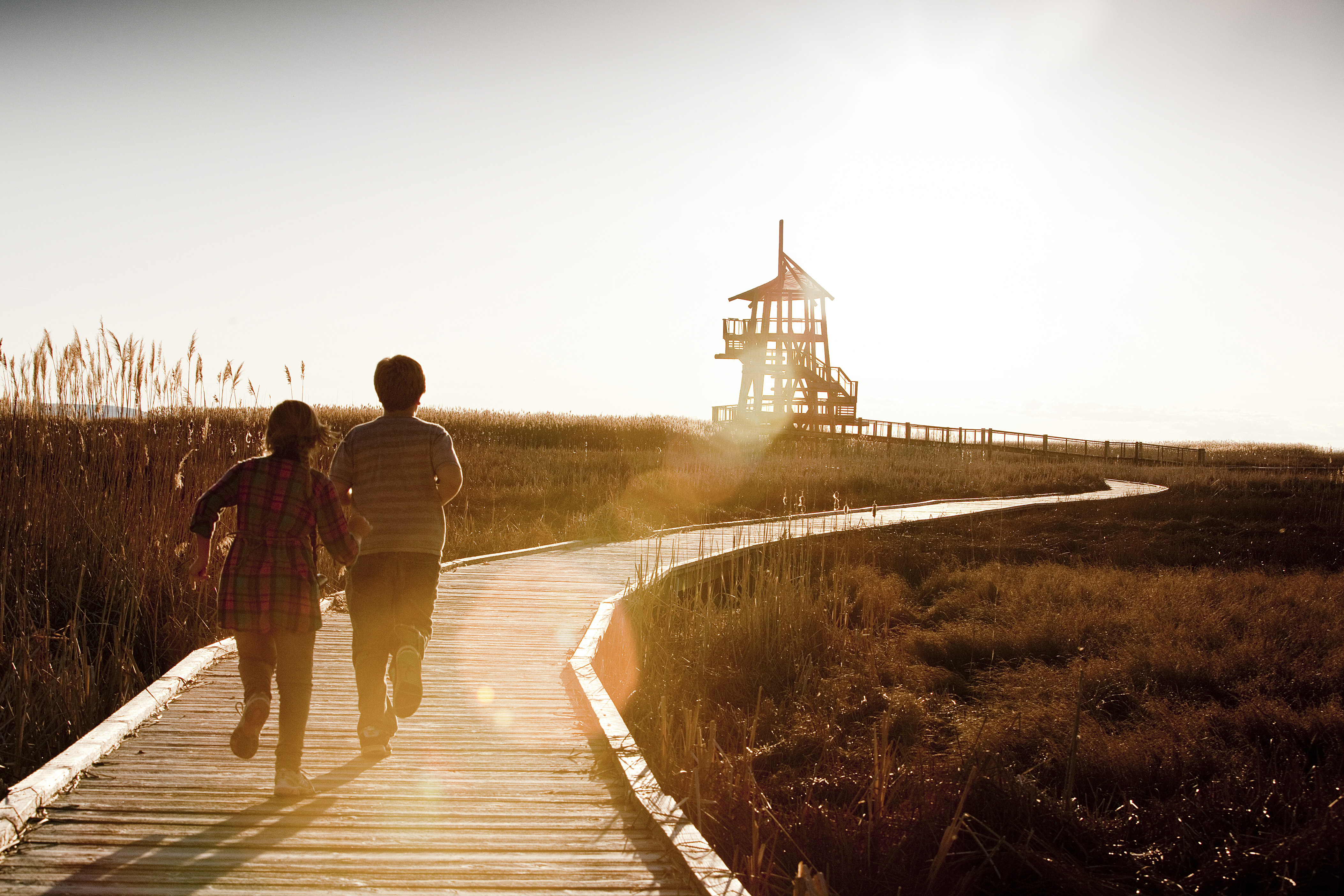 Two people run down a wooden boardwalk towards a tower.
