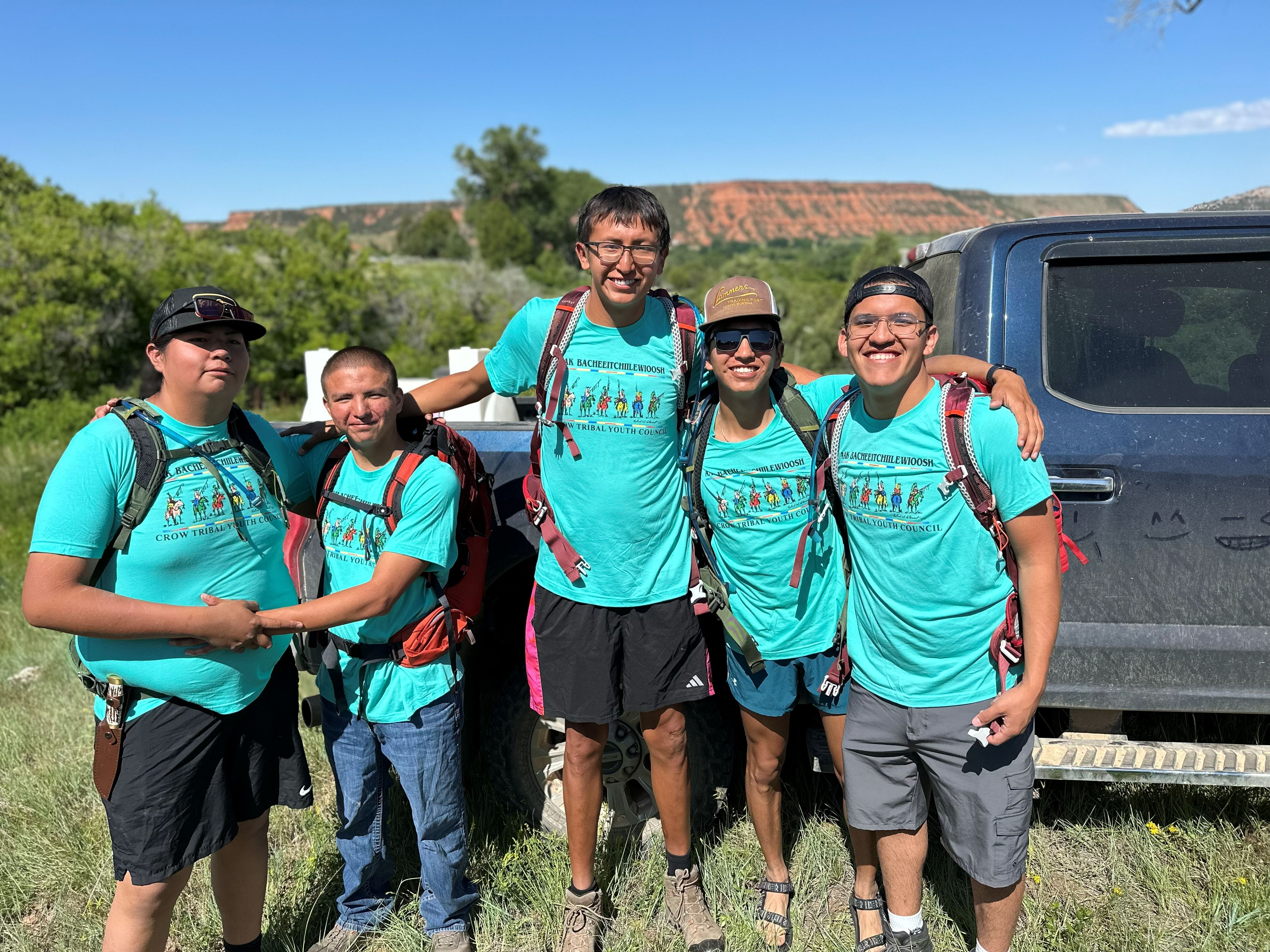 5 youth in matching shirts pose for camera.